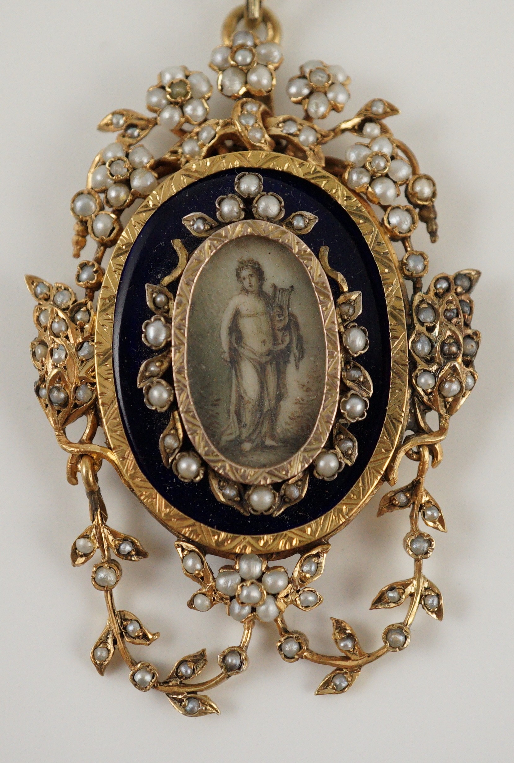 A Regency parcel gilt silver seed pearl and enamel set oval pendant, with inset ivory panel of a semi-clad figure with a lyre